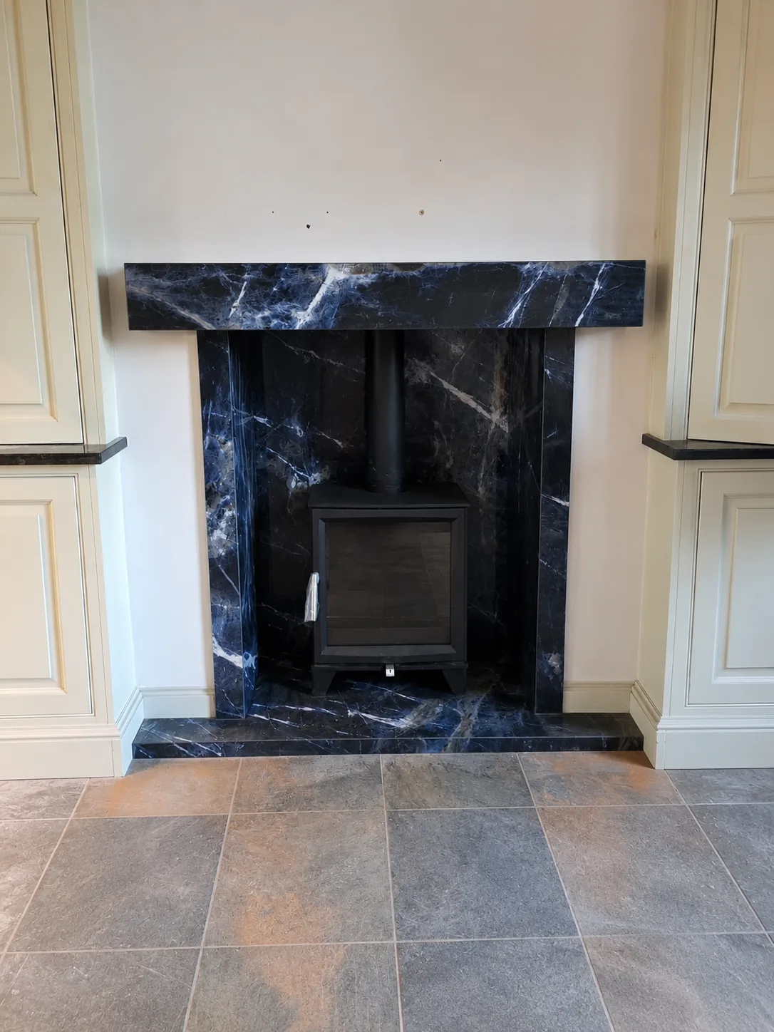 A bespoke Sodalite porcelain beam, stove hearth and chamber with striking blue and black veining framing a stove in an Olton home