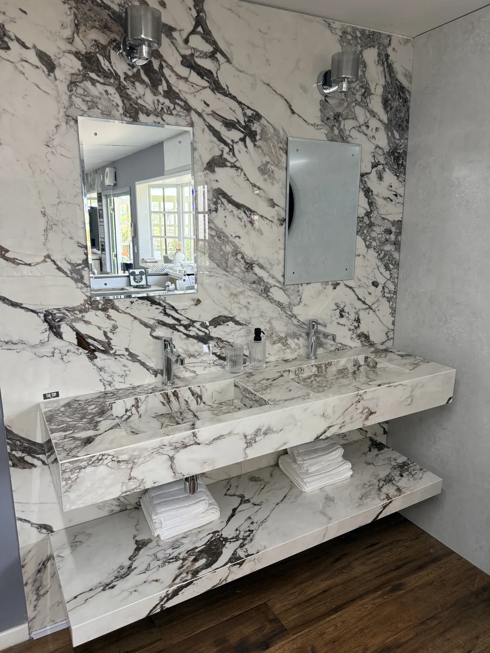 A full-height marble slab wall with a floating stone shelf and mirror in the Solihull showroom